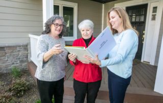 Three people standing in front of a home looking at a Home Assesssment notebook together.