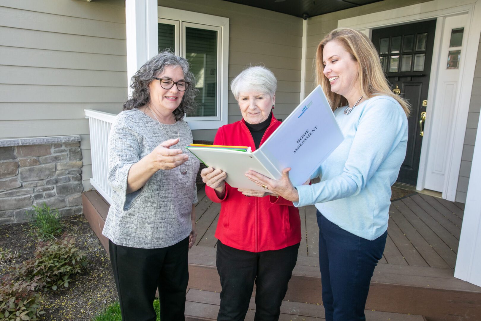 Three people standing in front of a home looking at a Home Assesssment notebook together.